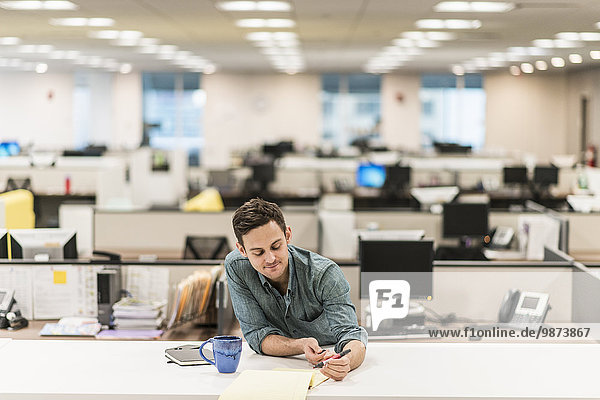 Ein junger Mann sitzt an einem Schreibtisch in einem Büro und hält einen Stift in der Hand.