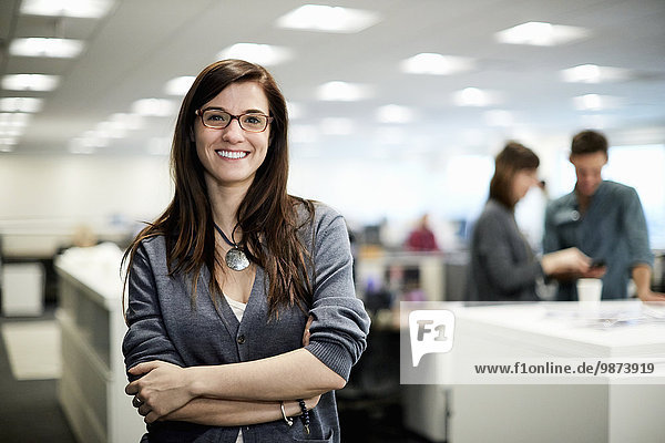 Eine Frau mit verschränkten Armen  lächelnd in einem Büro sitzend.