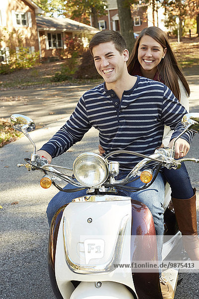 Couple riding scooter in suburban neighborhood