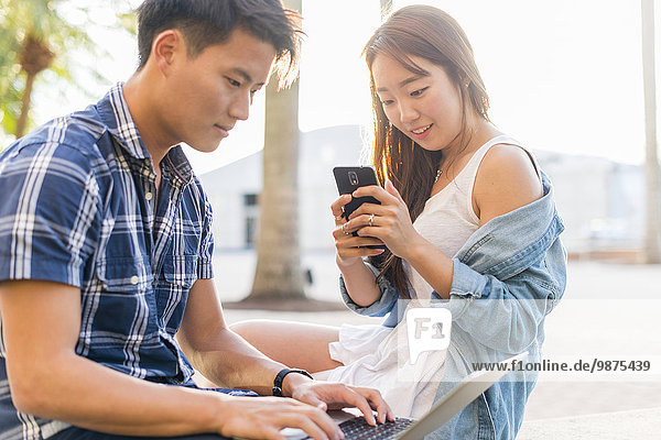Korean couple using laptop and cell phone outdoors
