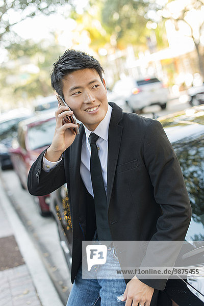 Korean businessman talking on cell phone near car