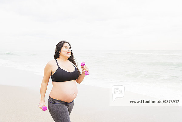 Pregnant mixed race woman exercising on beach