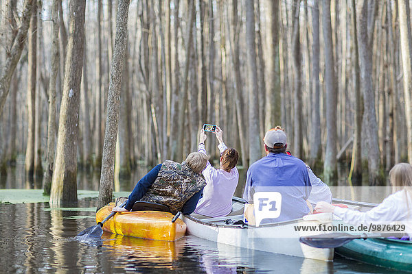 Caucasian family taking cell phone photographs in canoes on river