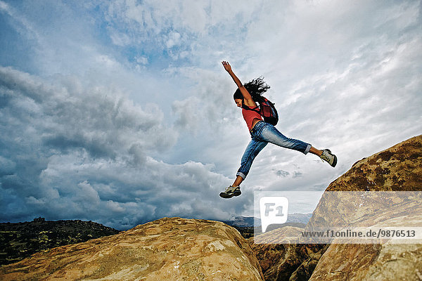 Hispanic woman jumping crevasse on rock formation