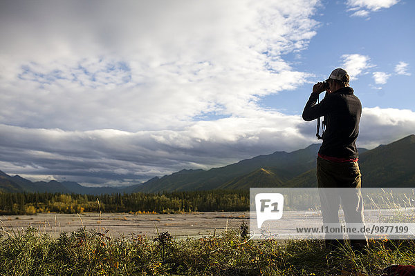 Man watches a braided riverbed with binoculars while hunting near Tok  Southcentral Alaska