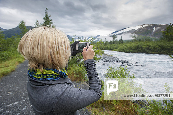 Woman using a smartphone to photograph Portage Creek  Portage Valley  Southcentral Alaska