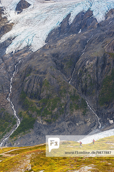 A man and woman hiking down the Harding Icefield Trail with Exit Glacier in the background  Kenai Fjords National Park  Kenai Penninsula  Southcentral Alaska