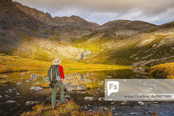 A man hiking stops to look at Lower Hidden Lake in the Chugach State Park on a autumn day in Southcentral Alaska.