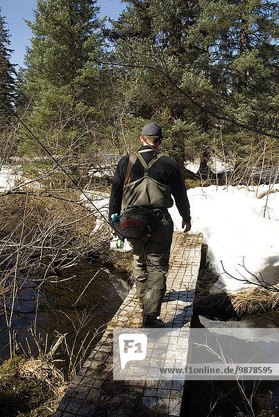 Fisherman Hiking Across A Small Bridge Along The Situk River During Early Spring In Southeast Alaska