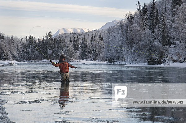 A Fly Fisherman Cast His Line Into The Kenai River As Ice Flows By During Winter In Alaska.