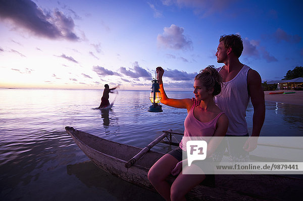 'Two tourists sitting at the water's edge at sunset; Savaii Island  Samoa'