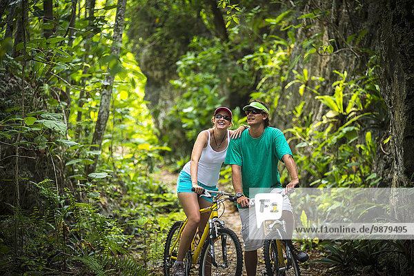 'A couple riding their bicycles on a trail through a lush forest; Niue'