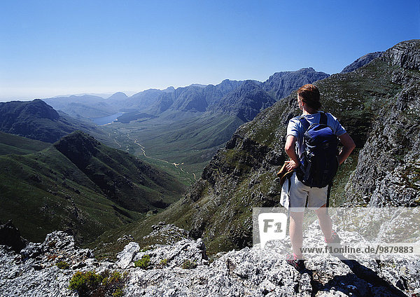 A Man With A Backpack Stands On A Mountain Ridge Looking Out Over The Valley And Range