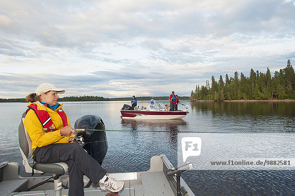 'A woman in her boat and a family in another boat all fish on a lake in Northern Ontario; Ontario  Canada'