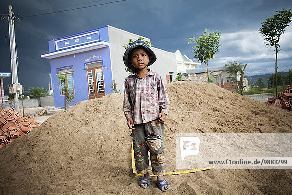 'A Hill Tribe vietnamese boy plays in a pile of sand with a tape measure; Dalat  Vietnam'