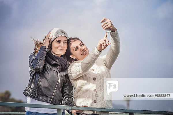Zwei junge Freundinnen mit Touchscreen für Smartphone Selfie an der Küste