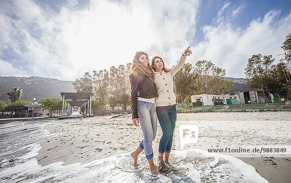 Two young women friends strolling barefoot on beach