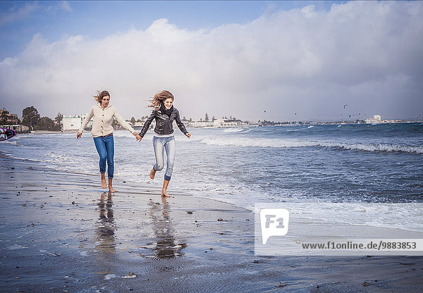 Zwei junge Frauen  die Hand in Hand am Strand laufen.