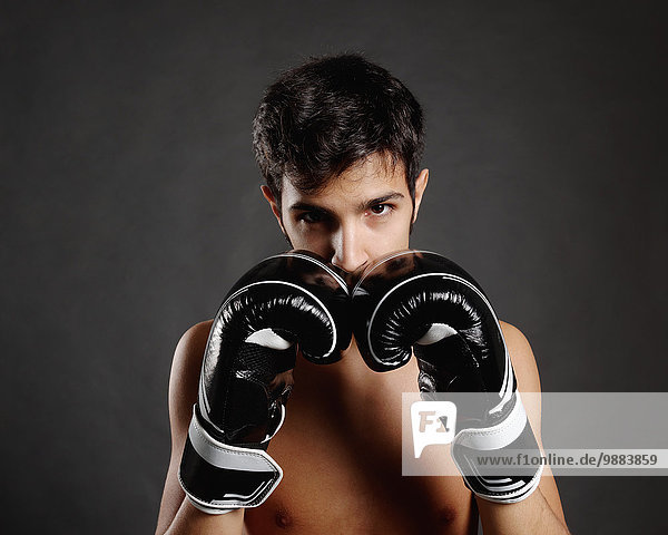Studio portrait of young man with boxing gloves in front of face