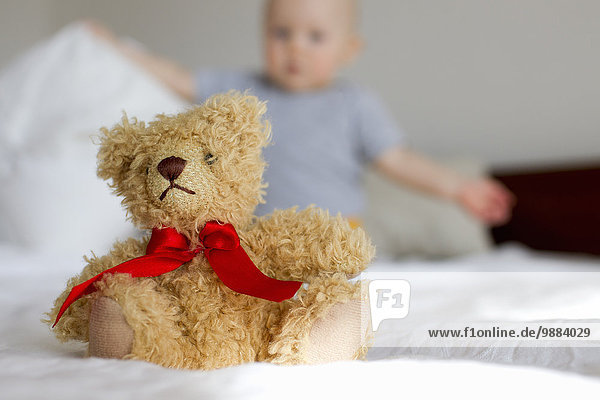 Süßer Teddybär im Bett sitzend vor dem kleinen Mädchen