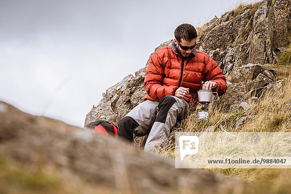 Young male hiker igniting camping stove  The Lake District  Cumbria  UK