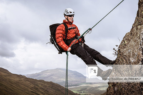 Young male climber abseiling down rock  The Lake District  Cumbria  UK