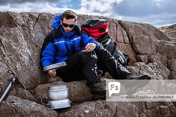 Junger Kletterer auf Felsen  der den Campingkocher vorbereitet  The Lake District  Cumbria  UK