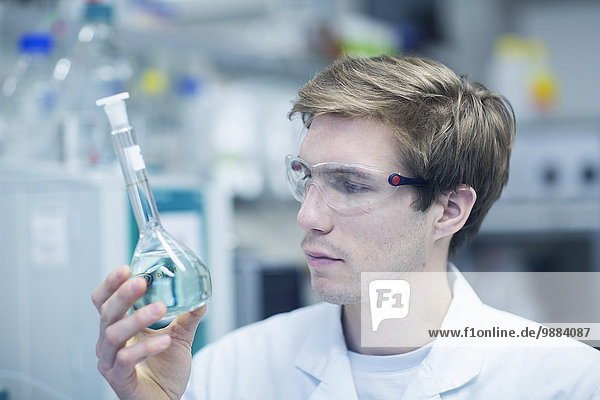 Männlicher Wissenschaftler hält sich hoch und schaut sich die Flasche im Labor an.
