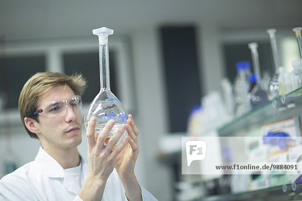 Männlicher Wissenschaftler hält Flasche im Labor hoch