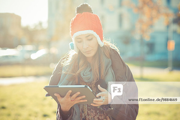 Mittlere erwachsene Frau in roter Pom Pom Mütze mit digitalem Tablett im Park