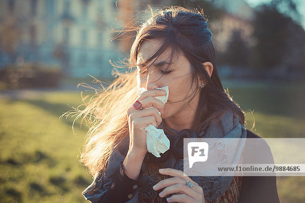 Mid adult woman blowing nose with handkerchief in park