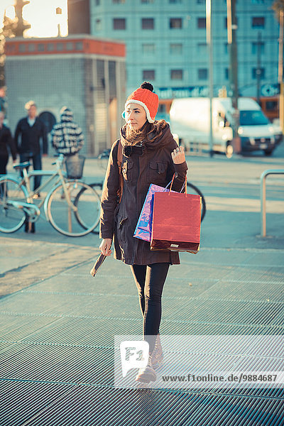 Mittlere erwachsene Frau mit rotem Bommelhut und Einkaufstaschen
