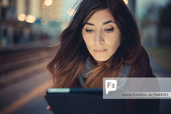 Mittlere erwachsene Frau mit digitalem Tablett-Touchscreen auf dem Bahnsteig in der Abenddämmerung