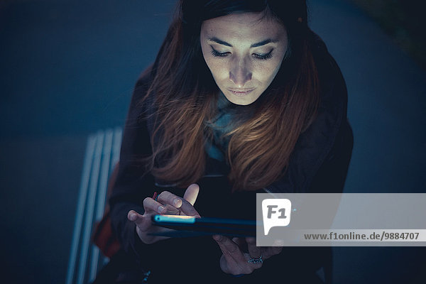 Mittlere erwachsene Frau mit digitalem Tablett-Touchscreen auf dem Bahnsteig in der Abenddämmerung