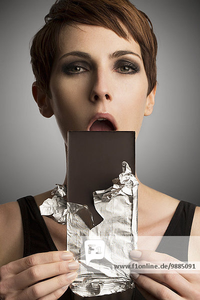 Studio-Porträt einer Frau  die dunkle Schokolade in den Mund hält.