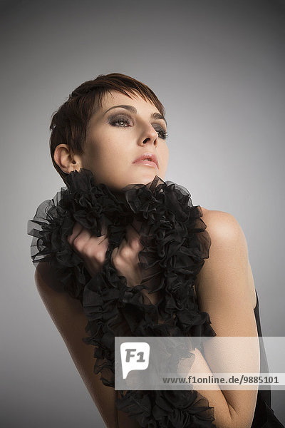 Studio-Porträt einer Frau  die eine schwarze Boa-Rüsche trägt und festhält.