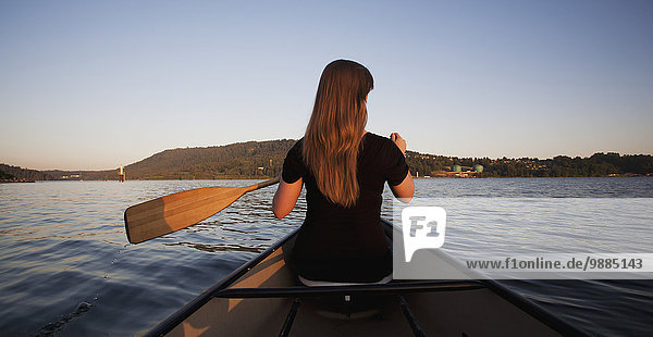A young woman canoeing at sunset; Vancouver  British Columbia  Canada