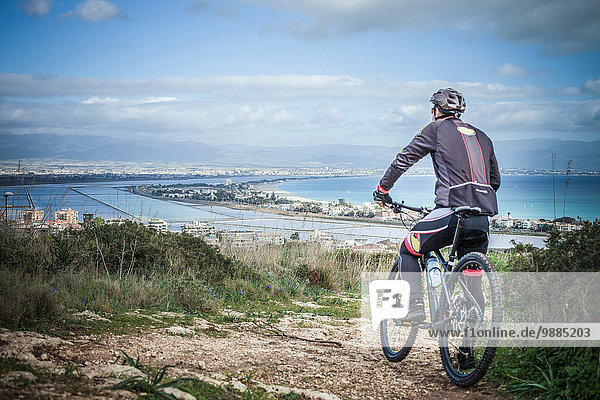 Rear view of male mountain biker looking out from coastal path  Cagliari  Sardinia  Italy