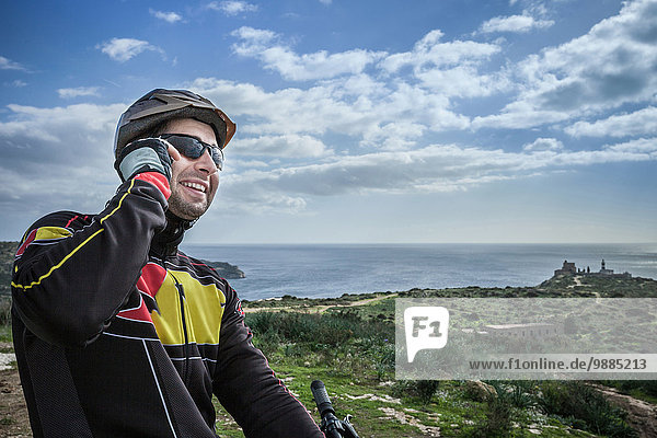 Mid adult male mountain biker chatting on smartphone from coastal path  Cagliari  Sardinia  Italy