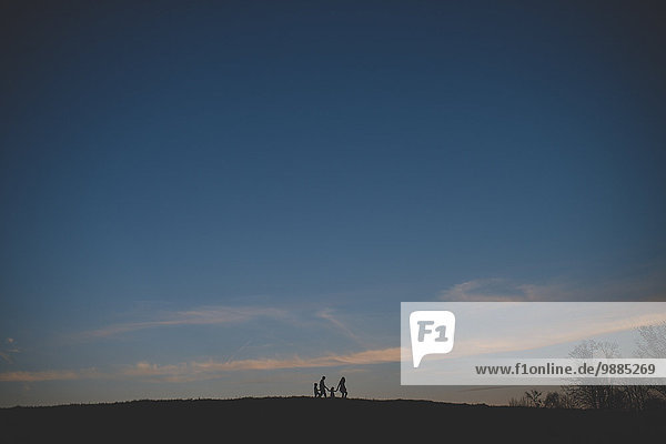 Scherenschnittansicht der Eltern mit Sohn und Tochter  die in der Abenddämmerung auf dem Hügel spazieren gehen.