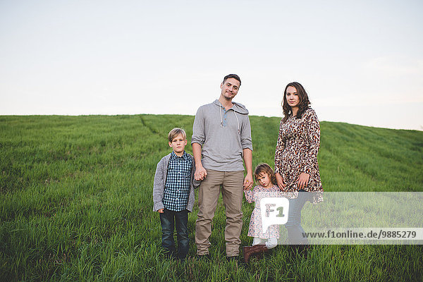 Portrait of young couple with son and daughter strolling in grassy field