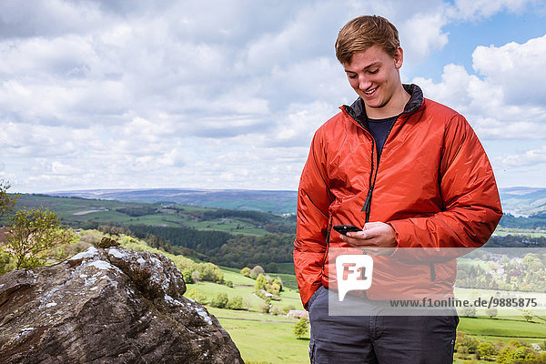 Männlicher Teenager-Wanderer beim Lesen von Smartphone-Texten auf Guise Cliff  Pateley Bridge  Nidderdale  Yorkshire Dales