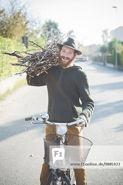 Junger Mann trägt einen Haufen Stöcke auf der Schulter auf dem Fahrrad.