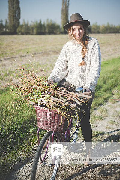 Young woman carrying bunch of sticks on bicycle