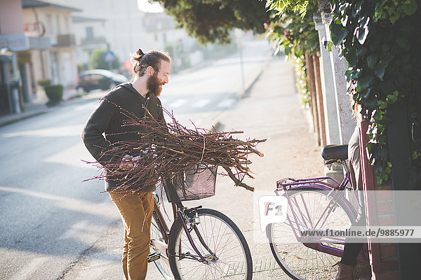 Young man carrying bunch of sticks on bicycle