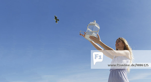 Junge Frau befreit Vogel aus dem Käfig in Richtung blauer Himmel