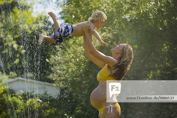 A pregnant mother plays in the water with her young son; Santa Barbara  California  United States of America