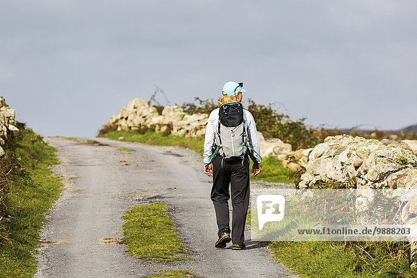 Female hiker walking along the road framed with stone fences; Omey Island  County Galway  Ireland