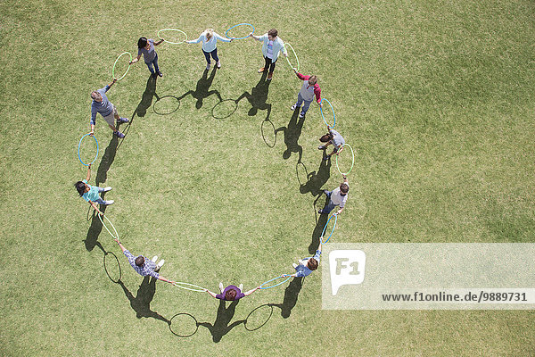 Team connected in circle by plastic hoops in sunny field