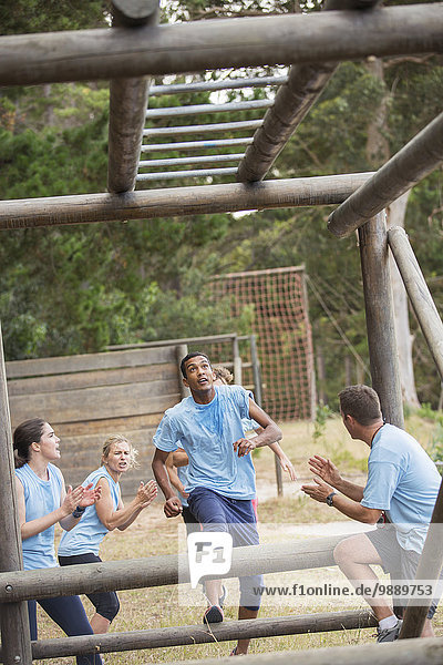 Teammates cheering for man nearing monkey bars on boot camp race course